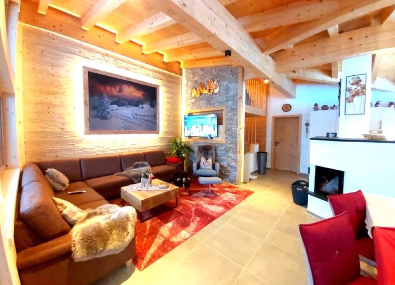 Gemütliche Wohnstube mit Kamin, Holzdecke und Ledersofa in einem JOWI-Chalet